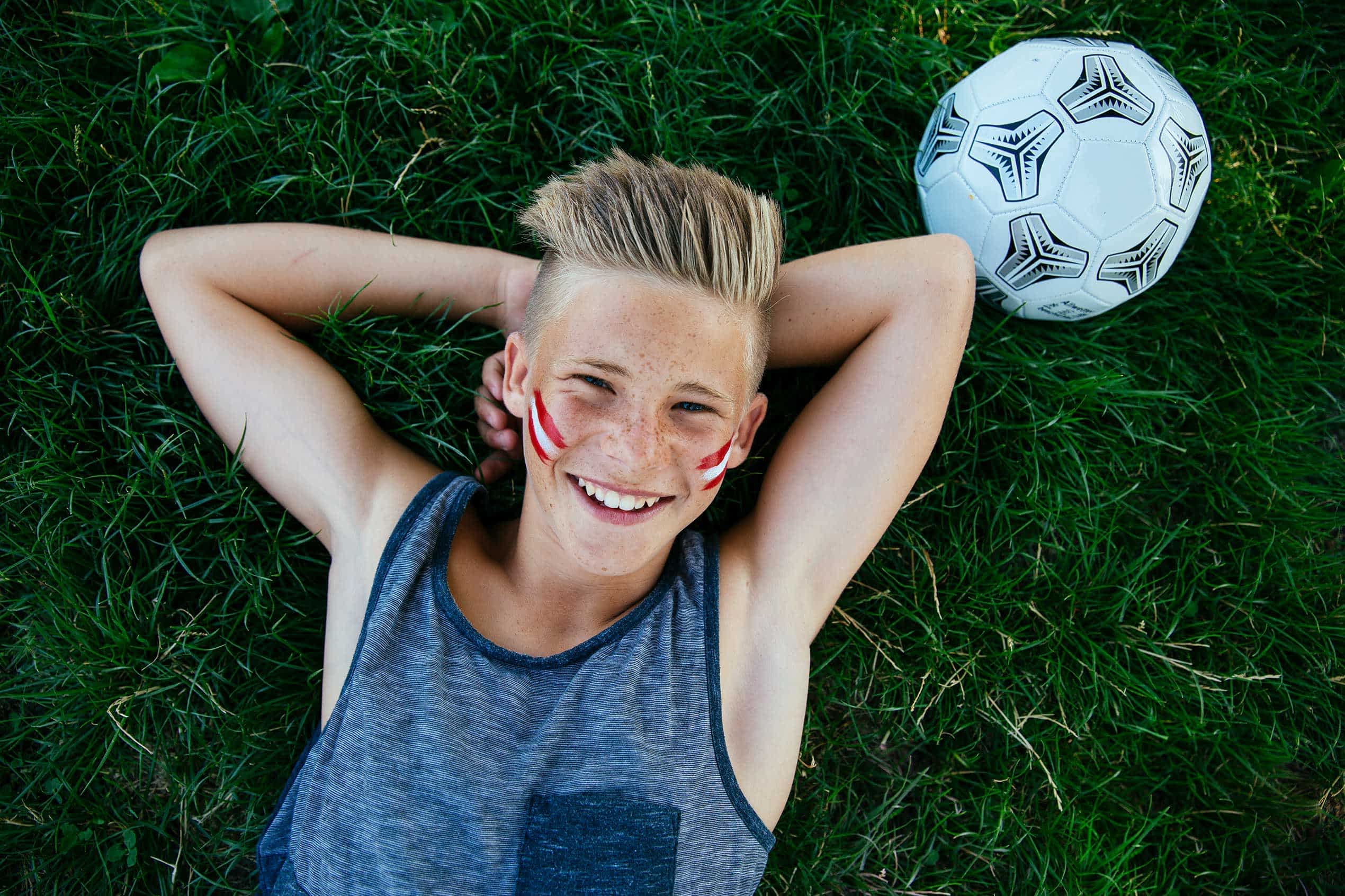 Kind mit Fußball liegt im Rasen für