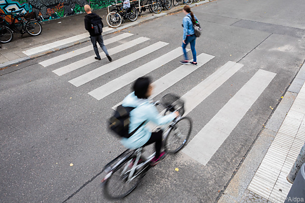 Auf dem Bild sieht man Fußgänger auf einem Zebrastreifen. Ein Fahrrad fährt auf der Straße.