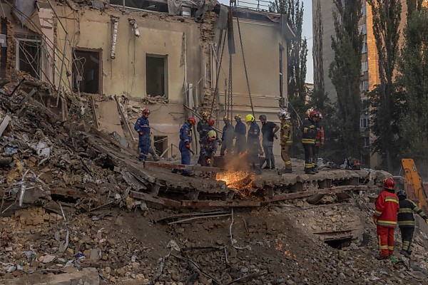 Auf dem Foto sieht man Teile des zerstörten Kinderspitals in Kiew. Davor stehen einige Männer, die nach Opfern suchen.