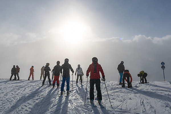 Auf dem Bild sieht man viele Urlauber in einem Ski-Gebiet. Man sieht auch die Sonne und das Wetter scheint sehr warm zu sein.