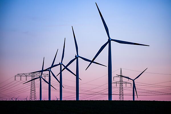 Auf dem Bild sieht man mehrere Windräder und Hochspannungsmasten.