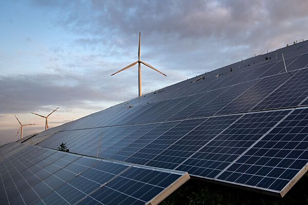 Auf dem Bild sieht man Windräder hinter einer Reihe von Solarzellen stehen.