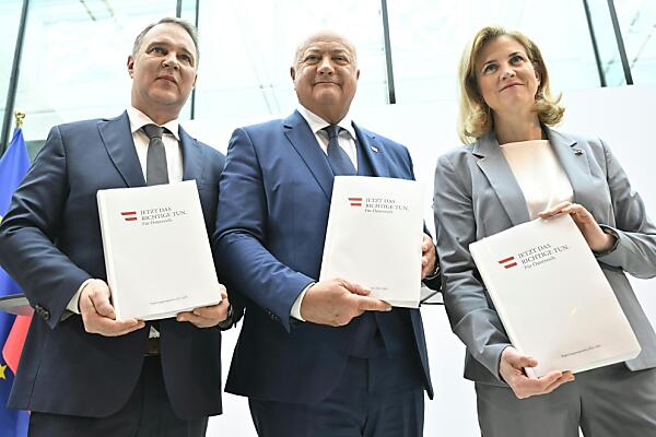 Auf dem Bild sieht man Andreas Babler, Christian Stocker und Beate Meinl-Reisinger. Sie stehen nebeneinander und halten das Regierungsprogramm in den Händen.