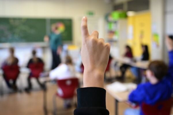 Auf dem Bild sieht man ein Kind in einem Klassenzimmer. Es zeigt gerade mit der Hand auf.