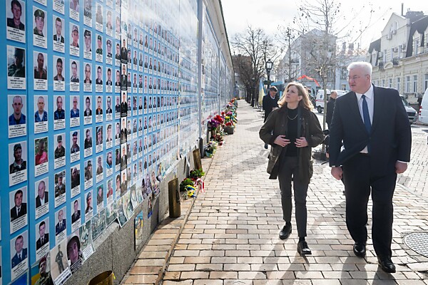 Auf dem Bild sieht man Außenministerin Beate Meinl-Reisinger und ihren ukrainischen Kollegen. Sie gehen die Gedenkmauer mit Bildern von gefallenen Soldaten entlang.