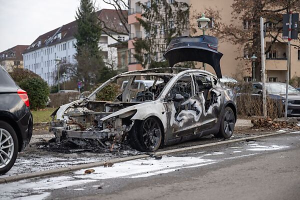 Auf dem Bild sieht man einen ausgebrannten Tesla an einem Straßenrand in Berlin stehen.