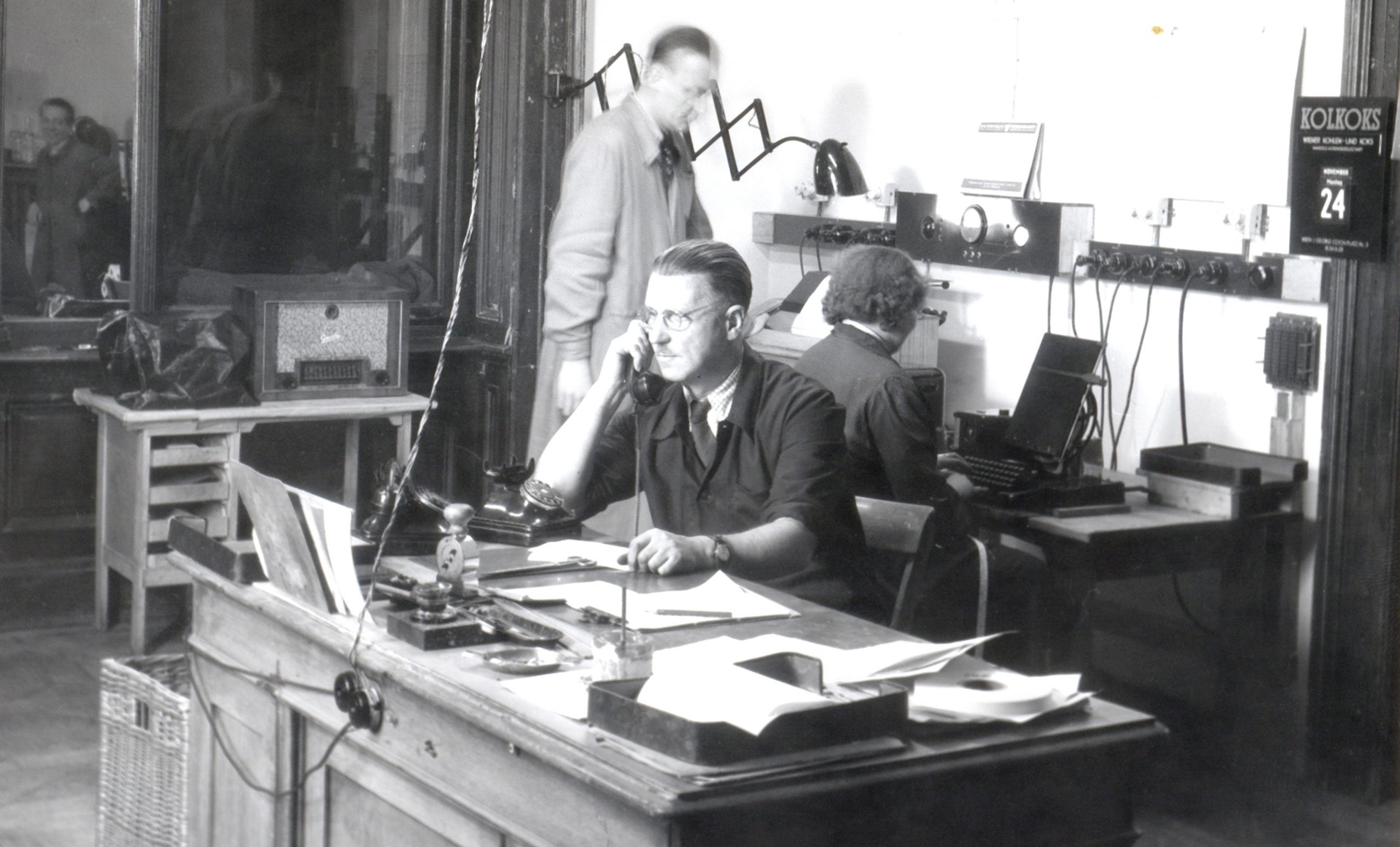 Ein historisches schwarz-weiß Foto aus der APA, ein Redakteur telefoniert mit einem alten Telefon