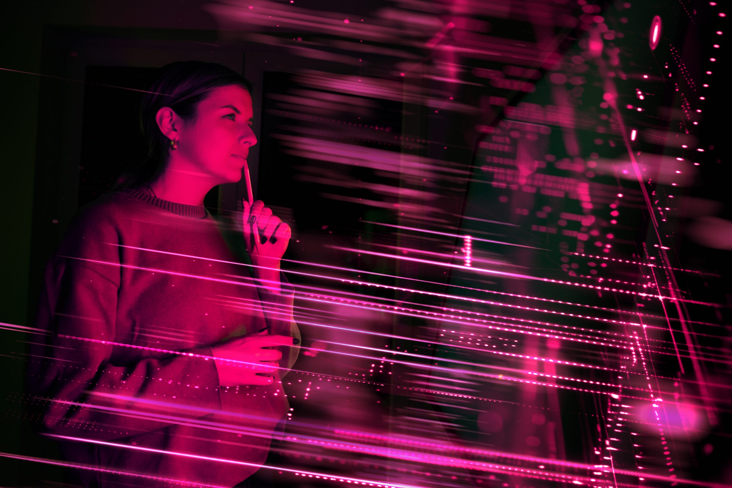 Foto einer jungen Frau, die von pinken Neon-Lichtern umgeben ist und nachdenklich einen Bleistift zum Mund führt.