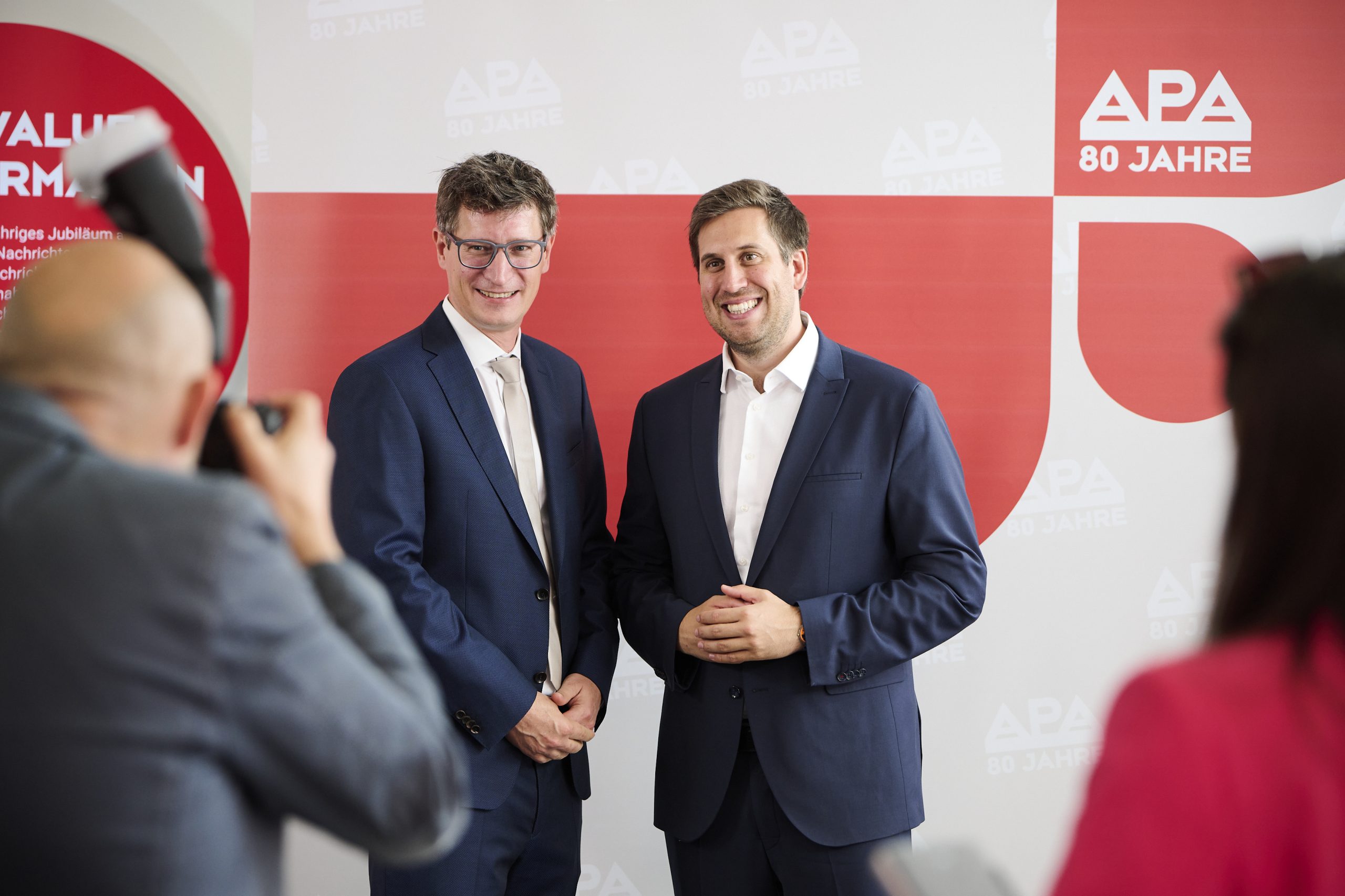 Zwei Männer stehen vor einer Fotowand und werden fotografiert