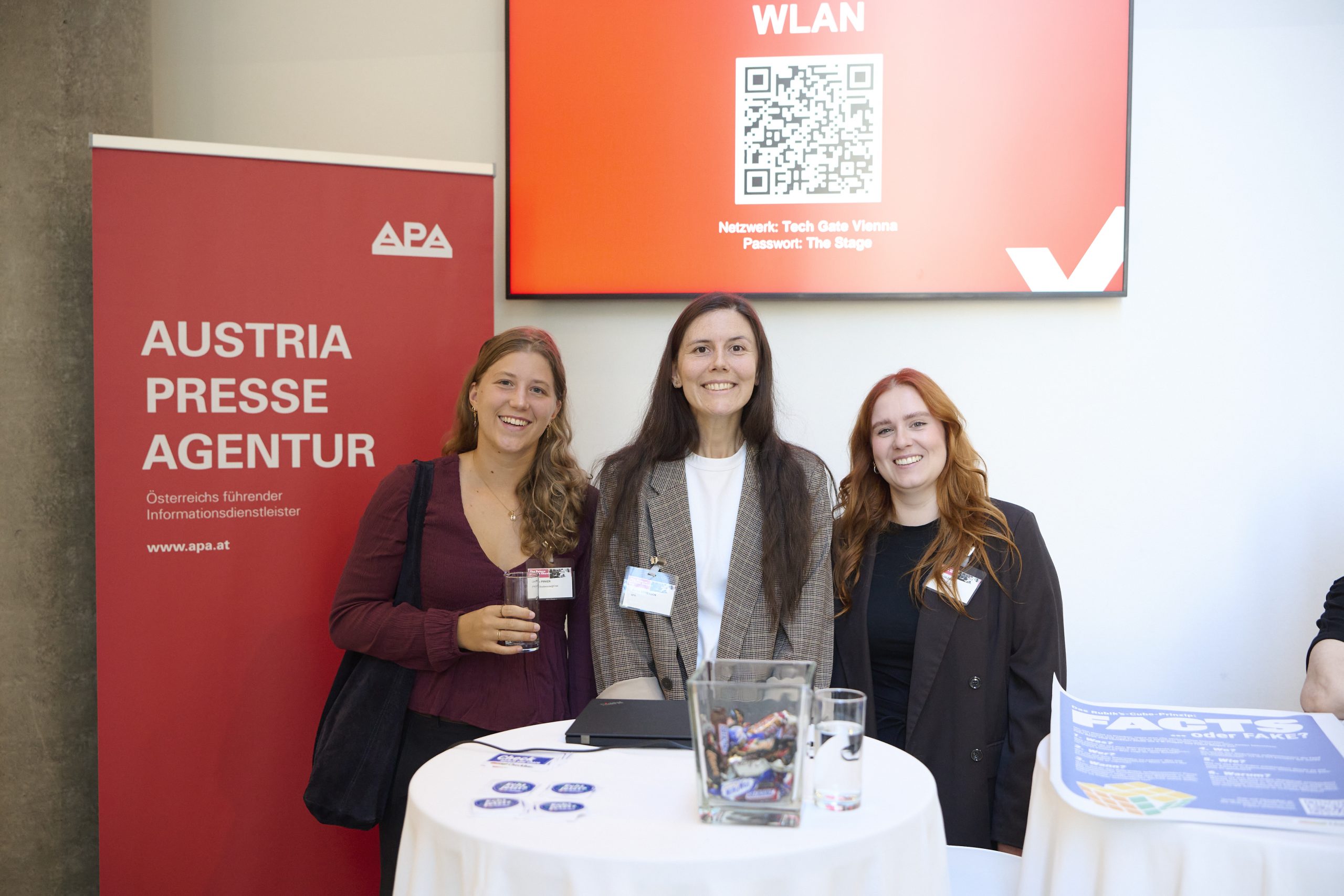 Drei Frauen stehen hinter einem Stehtisch und posieren für ein Foto