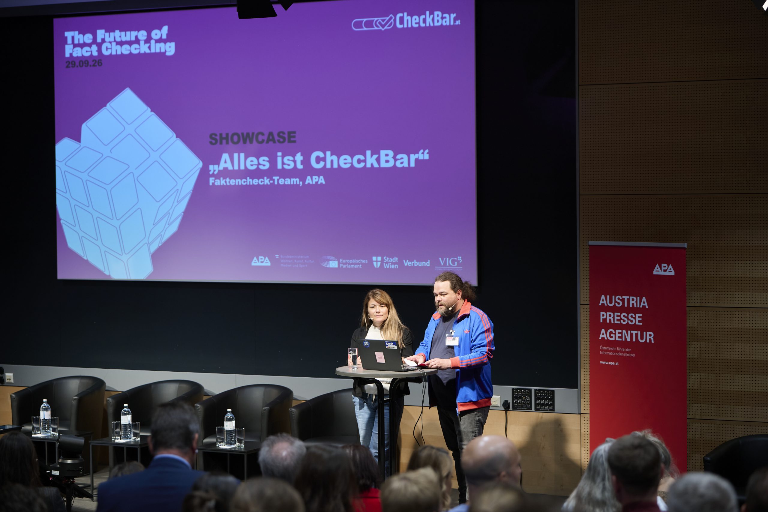 Ein Mann und eine Frau präsentieren auf einer Bühne das Projekt "CheckBar"